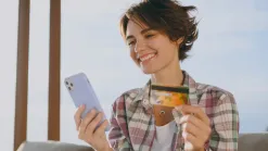 Usmiata žena vonku drží v ruke mobil a platobnú kartu