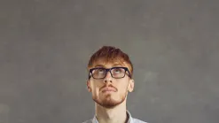 Mladý muž s okuliarmi zamyslene hľadí nahor