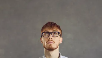 Mladý muž s okuliarmi zamyslene hľadí nahor
