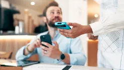 Obsluha podáva hosťovi v kaviarni platobný terminál, muž drží v ruke mobil