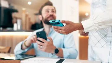Obsluha podáva hosťovi v kaviarni platobný terminál, muž drží v ruke mobil