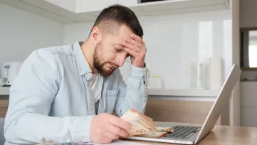 Mladší muž s peniazmi v ruke sa ustarostene pozerá pred seba