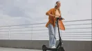 usmiata žena so slúchadlami na elektrickej kolobežke na promenáde pri zábradlí