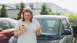 Žena s mobilom a kľúčmi od auta stojí na parkovisku pred svojím vozidlom
