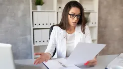 Žena v kancelárii prekvapene číta dokument, na stole doklady a laptop