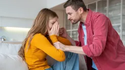 Muž sa nakláňa nad plačúcou ženou na pohovke a drží ju za ruku