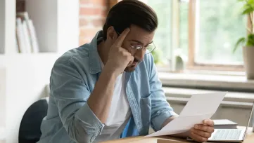 Muž pri laptope si drží hlavu a hľadí na list z úradu