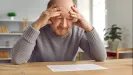Muž si drží hlavu oboma rukami nad dokumentom na stole