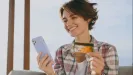 Usmiata mladá žena vonku drží mobil a platobnú kartu