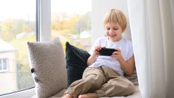 Usmiaty chlapec pri okne hrá na smartfóne