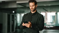 Muž v košeli píše na mobile v presklenej kancelárii