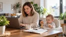 mladá mama v béžovom svetri pracuje doma na notebooku, vedľa nej bábätko v detskej stoličke sa hrá s drevenou hračkou