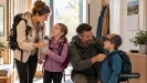 rodina v predsieni s batohmi sa chystá na výlet, mama podáva dcére fľašu, otec synovi zapína batoh, na stene kalendár